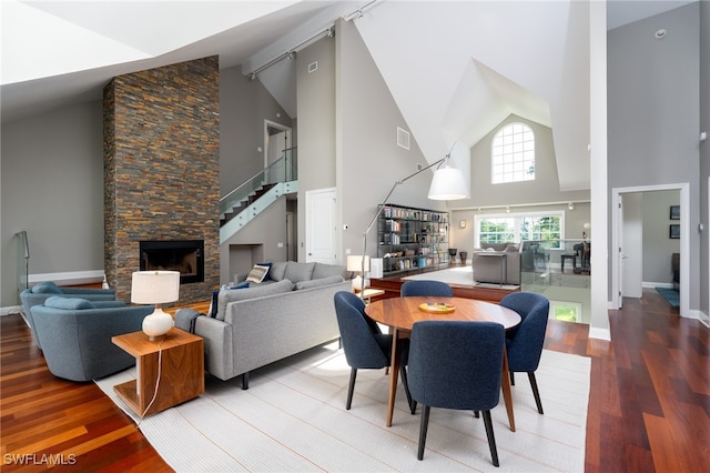 dining area featuring a fireplace, wood-type flooring, and high vaulted ceiling