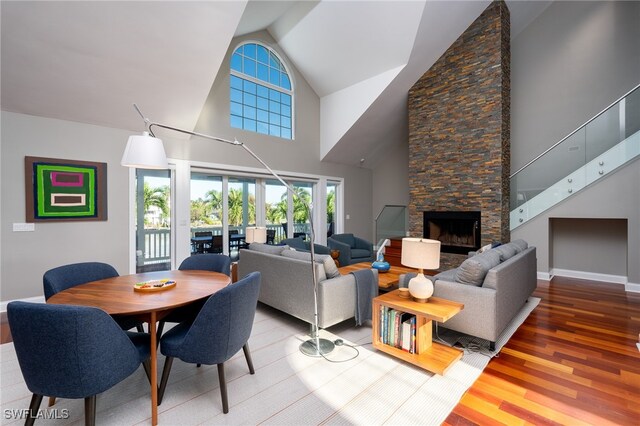 living room featuring high vaulted ceiling, a stone fireplace, and wood-type flooring