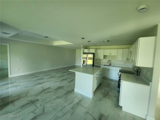 kitchen featuring stainless steel fridge, a kitchen island, white cabinetry, sink, and decorative light fixtures