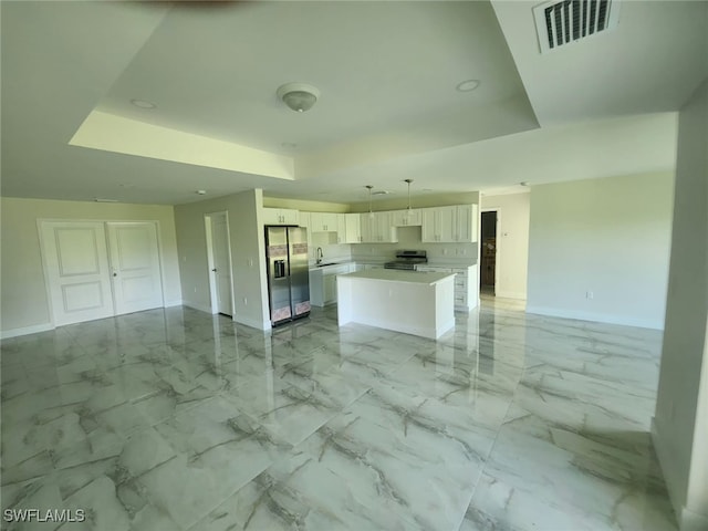 kitchen with a kitchen island, decorative light fixtures, stainless steel appliances, and a tray ceiling