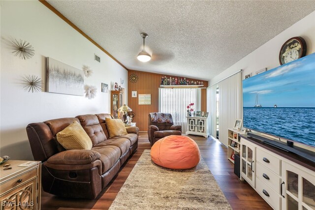 living room featuring a textured ceiling, dark wood-type flooring, lofted ceiling, wooden walls, and ornamental molding