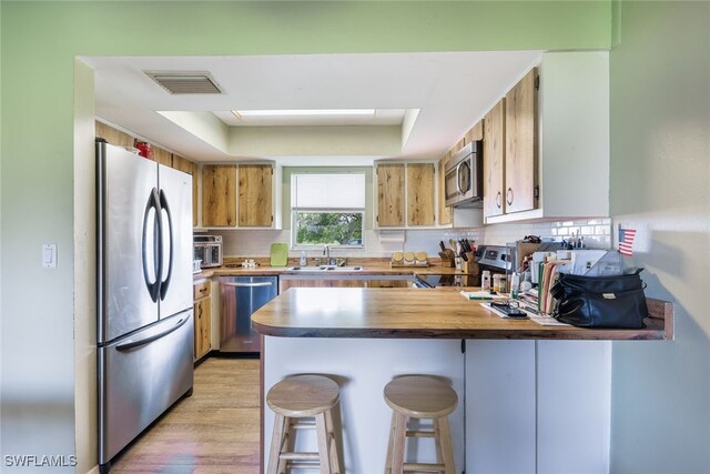 kitchen with sink, kitchen peninsula, appliances with stainless steel finishes, a breakfast bar, and light wood-type flooring