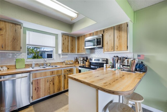 kitchen featuring appliances with stainless steel finishes, backsplash, sink, and wood counters