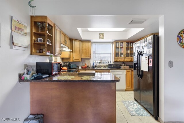 kitchen featuring black appliances, kitchen peninsula, light tile patterned flooring, and a raised ceiling