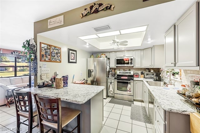 kitchen with a kitchen bar, backsplash, stainless steel appliances, a tray ceiling, and sink