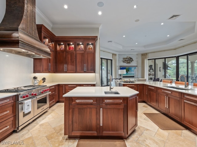 kitchen featuring sink, an island with sink, custom range hood, and range with two ovens