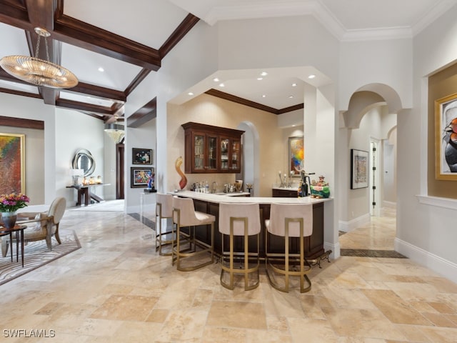 bar featuring a towering ceiling, ornamental molding, beam ceiling, and a chandelier