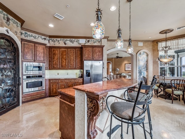 kitchen featuring a center island with sink, ceiling fan, appliances with stainless steel finishes, crown molding, and decorative light fixtures