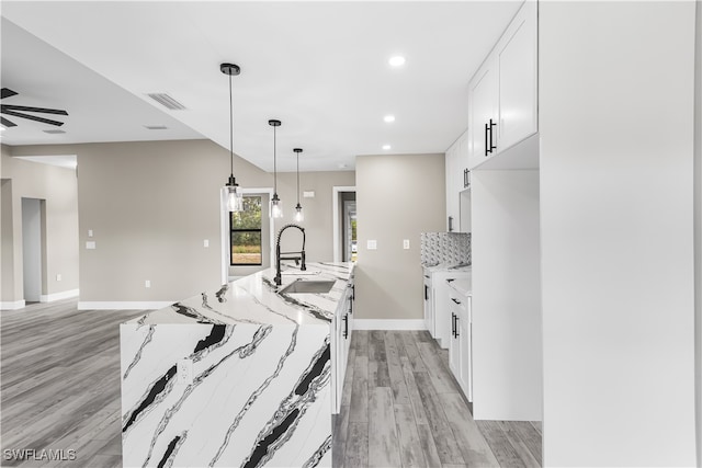 kitchen with light hardwood / wood-style floors, light stone counters, tasteful backsplash, white cabinets, and sink