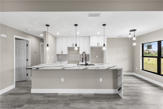 kitchen with light stone countertops, white cabinetry, hanging light fixtures, and a spacious island