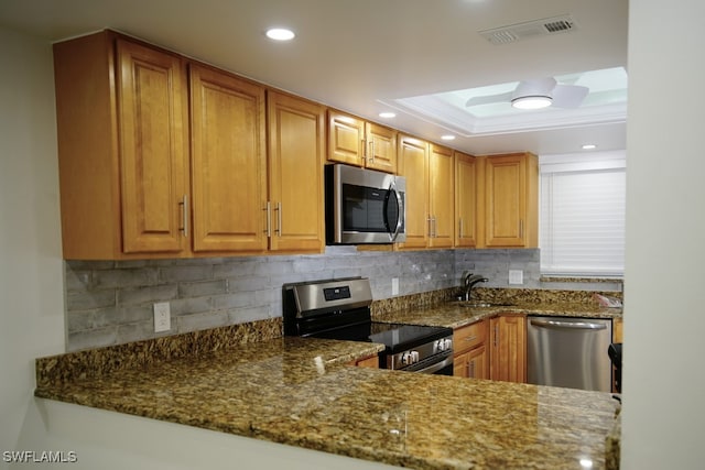 kitchen featuring backsplash, a raised ceiling, sink, dark stone countertops, and stainless steel appliances