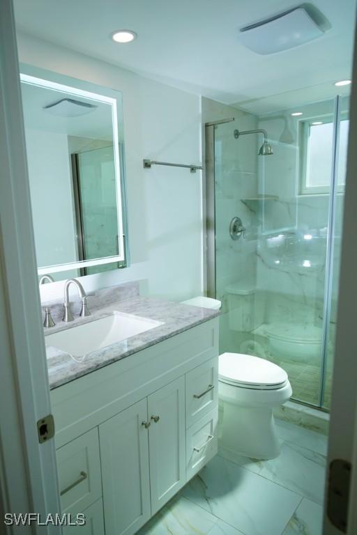 bathroom with a shower with door, vanity, and toilet