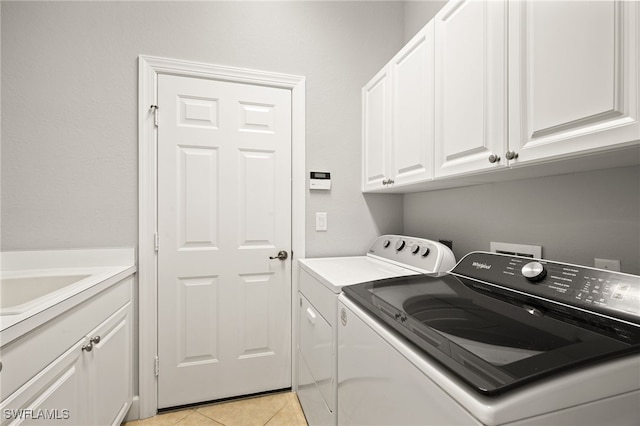 clothes washing area with washer and clothes dryer, cabinets, and light tile patterned floors