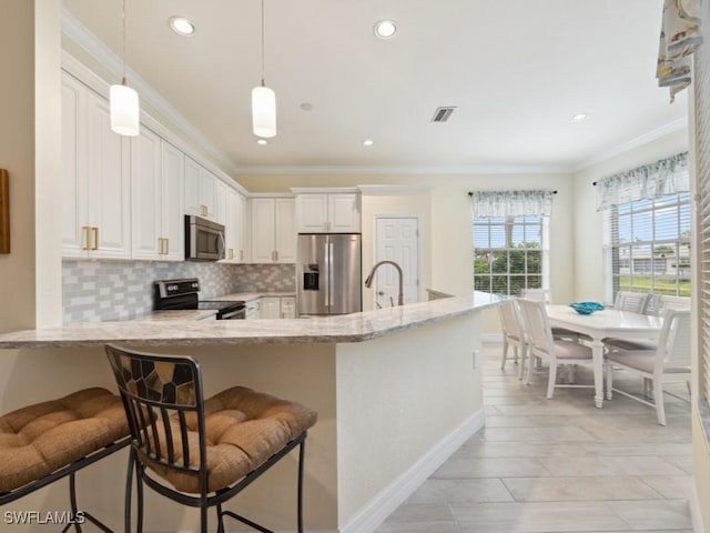 kitchen featuring pendant lighting, appliances with stainless steel finishes, light stone counters, white cabinetry, and a breakfast bar area