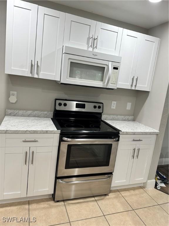 2611 4th St SW, Lehigh Acres, FL 33976 - kitchen featuring stainless steel range with electric cooktop, white microwave, light tile patterned floors, and white cabinets