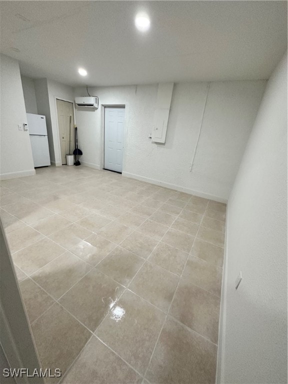 basement with white refrigerator, light tile patterned floors, and a wall unit AC