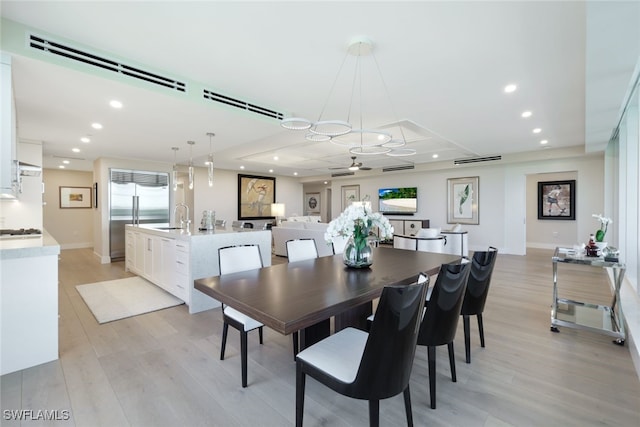 dining area featuring sink, a tray ceiling, light wood-type flooring, and ceiling fan