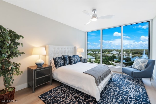 bedroom with a water view, ceiling fan, wood-type flooring, and multiple windows