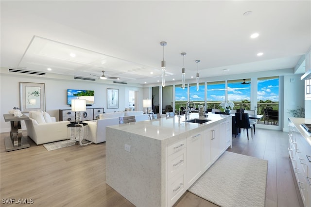 kitchen featuring light hardwood / wood-style floors, hanging light fixtures, an island with sink, and white cabinets