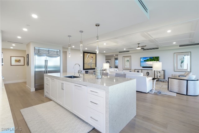 kitchen featuring hanging light fixtures, white cabinetry, light hardwood / wood-style floors, built in refrigerator, and a kitchen island with sink