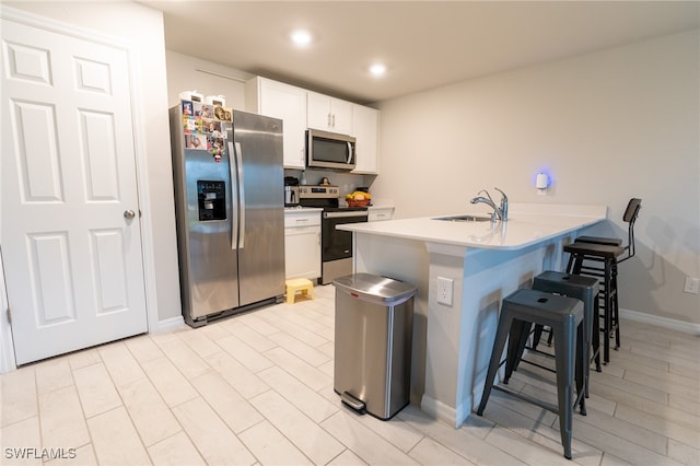 kitchen with appliances with stainless steel finishes, a breakfast bar, sink, and white cabinetry