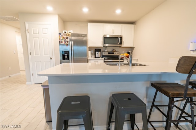 kitchen featuring stainless steel appliances, white cabinets, sink, light hardwood / wood-style flooring, and a kitchen bar