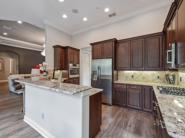 kitchen with hardwood / wood-style flooring, stainless steel appliances, ornamental molding, light stone counters, and tasteful backsplash