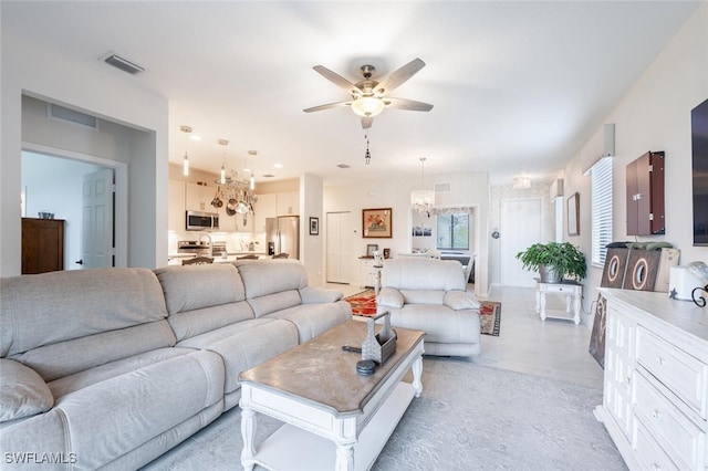 tiled living room with ceiling fan with notable chandelier