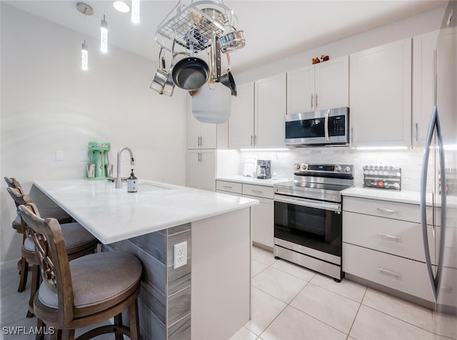 kitchen featuring stainless steel appliances, sink, pendant lighting, light tile patterned floors, and white cabinets