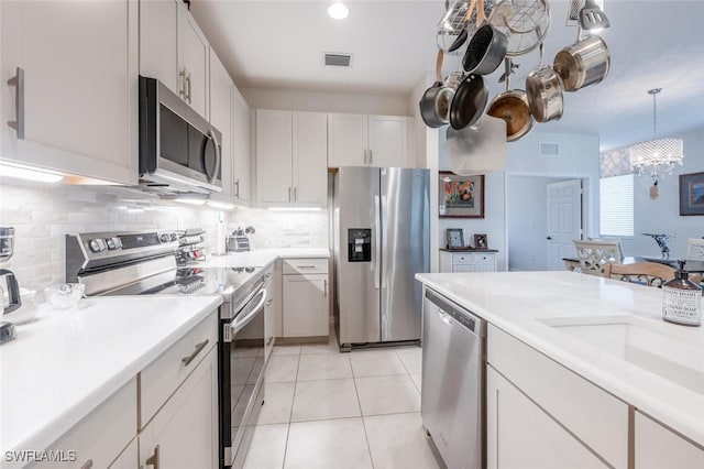 kitchen featuring decorative backsplash, appliances with stainless steel finishes, light tile patterned flooring, white cabinetry, and a chandelier