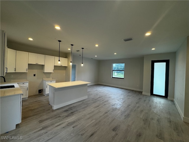 kitchen with hanging light fixtures, sink, white cabinetry, a center island, and light wood-type flooring