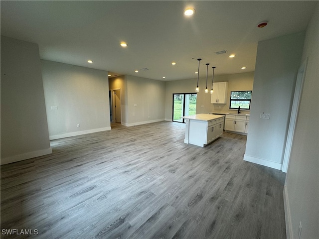 kitchen featuring light wood-type flooring, a kitchen island, decorative light fixtures, sink, and white cabinets