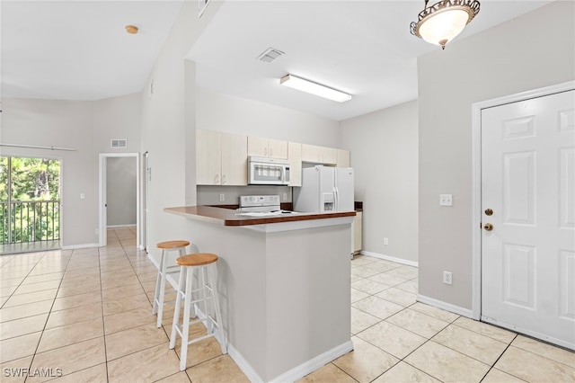 kitchen with kitchen peninsula, white appliances, light tile patterned floors, and a breakfast bar