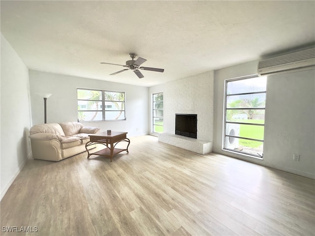 living room featuring a fireplace, light wood-type flooring, a wall mounted air conditioner, and ceiling fan