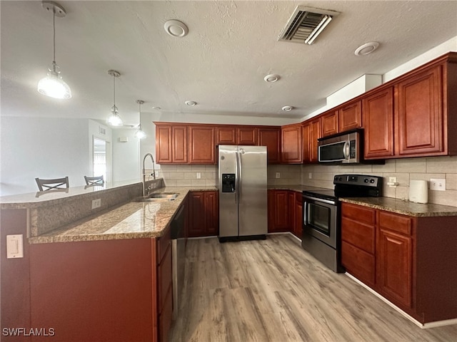 kitchen featuring sink, hanging light fixtures, light hardwood / wood-style floors, kitchen peninsula, and stainless steel appliances