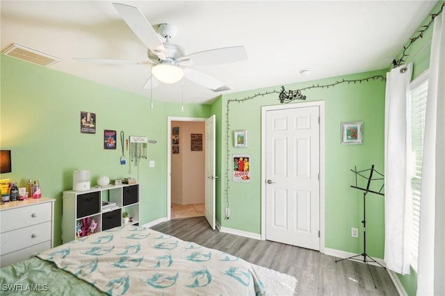 bedroom featuring ceiling fan, wood finished floors, visible vents, and baseboards