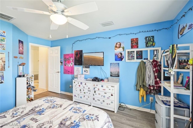 bedroom with a ceiling fan, wood finished floors, visible vents, and baseboards