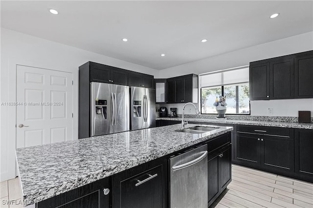 kitchen with a kitchen island with sink, light hardwood / wood-style flooring, light stone counters, sink, and appliances with stainless steel finishes