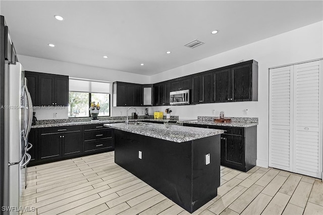 kitchen featuring light stone countertops, a kitchen island with sink, stainless steel appliances, sink, and light hardwood / wood-style floors