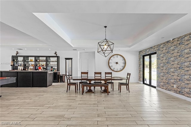 dining space with bar area, a tray ceiling, and light hardwood / wood-style floors