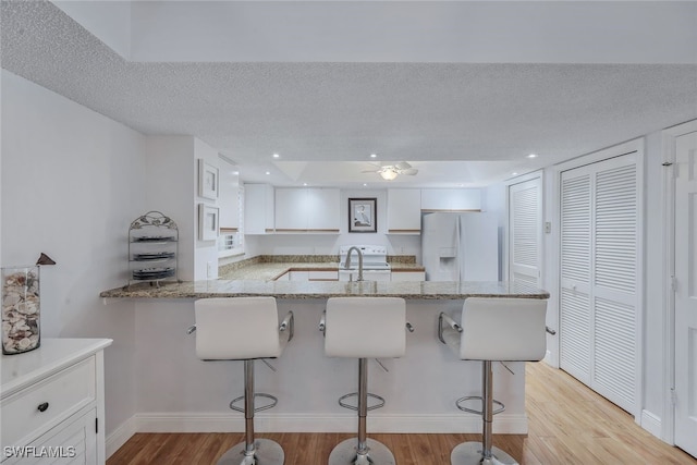 kitchen with white fridge with ice dispenser, kitchen peninsula, light hardwood / wood-style floors, white cabinets, and a breakfast bar