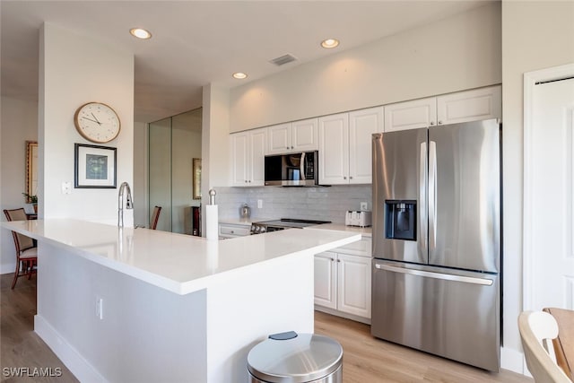 kitchen featuring backsplash, stainless steel appliances, light hardwood / wood-style flooring, white cabinetry, and an island with sink