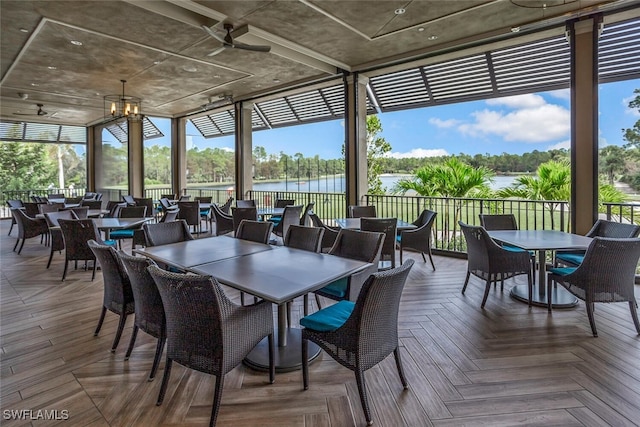 sunroom / solarium with a water view and ceiling fan with notable chandelier