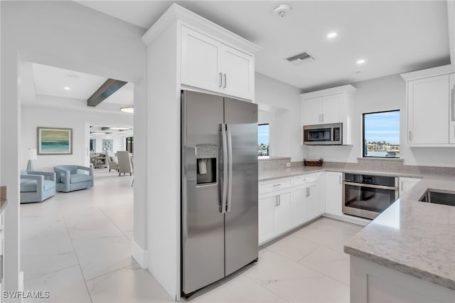 kitchen with appliances with stainless steel finishes, white cabinets, beam ceiling, and light stone counters