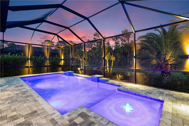 pool at dusk with glass enclosure, a patio, and pool water feature