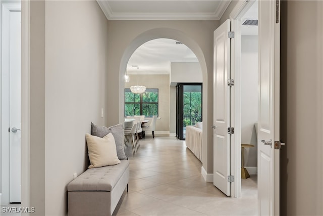 hallway with a notable chandelier, crown molding, and light tile patterned floors