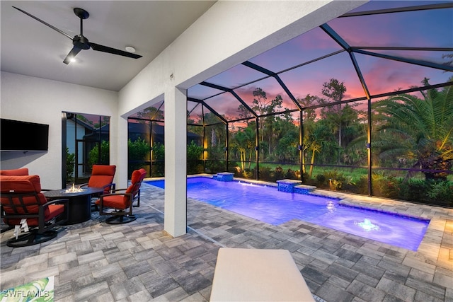 pool at dusk featuring ceiling fan, a jacuzzi, a patio area, a lanai, and pool water feature