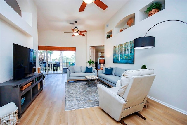 living room with ceiling fan, light wood-type flooring, and a high ceiling