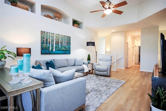 living room featuring hardwood / wood-style flooring, ceiling fan, and a towering ceiling