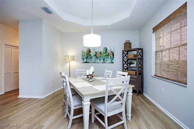 dining room with a raised ceiling and light wood-type flooring